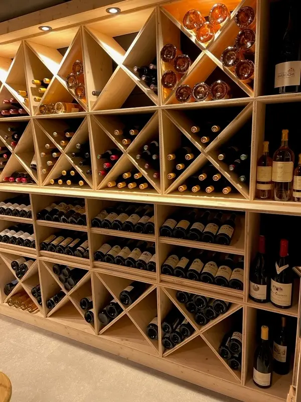 Mur de casiers à vin en bois clair garni de bouteilles, compartiments en croix en haut et en bas, rangées d'étagères au centre pour présenter les étiquettes